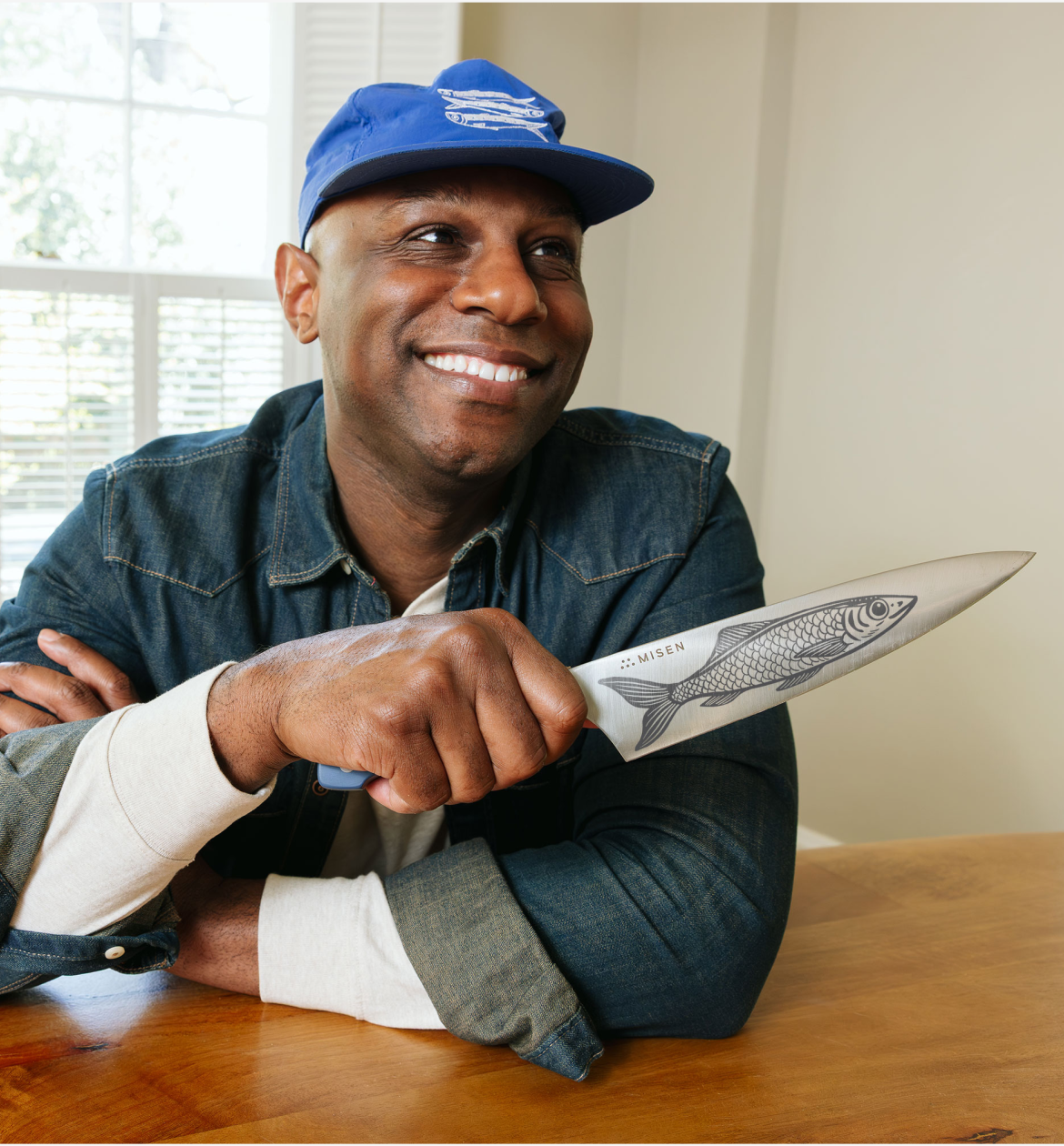 Man smiling holding Misen chef's knife with fish engraving wearing blue cap