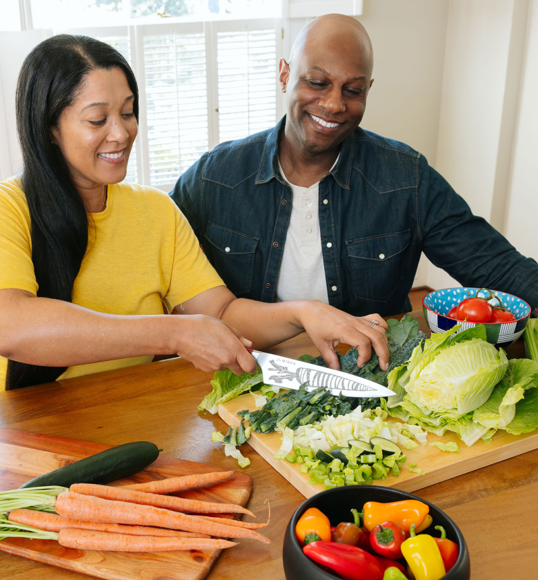 Couple smiling while chopping fresh vegetables together in kitchen